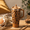 Gobelet isotherme Du Bruit dans la Cuisine Qwetch 900ml camel à motif léopard avec paille et poignée sur une table